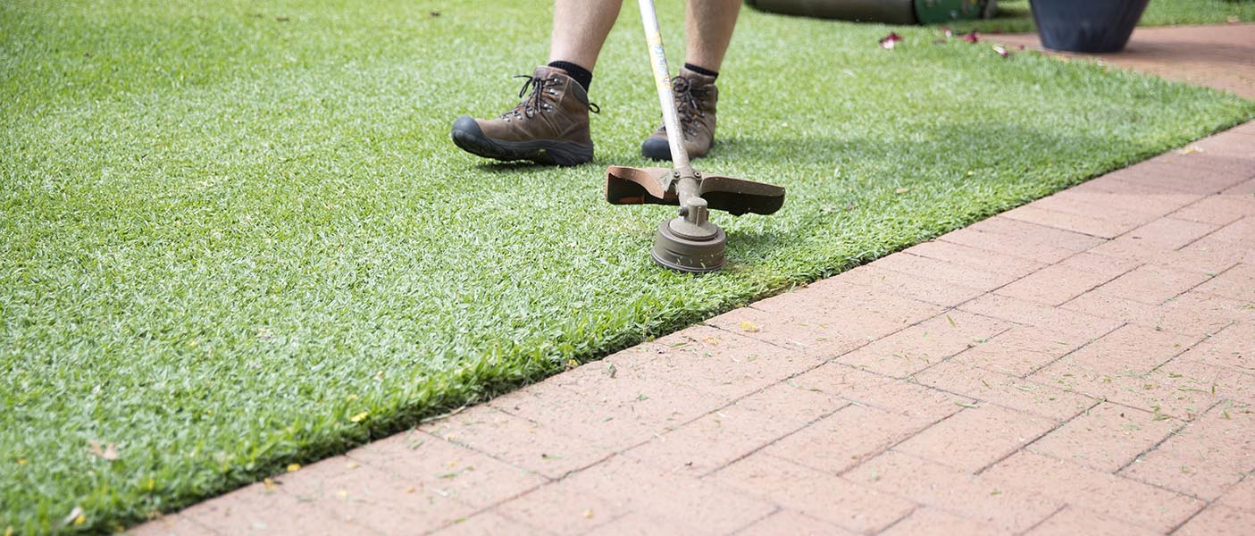 Gardener whipper snipping green lawn next to paving with whipper snipper/brush cutter for lawn mowing Dudley Park